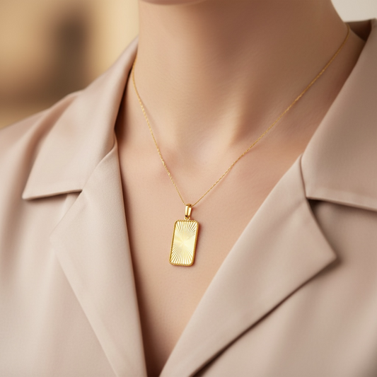 Woman wearing a beige coat with a gold necklace featuring a rectangular fluted sunburst pendant.