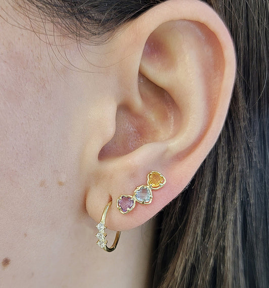 A close-up of a person's ear showcasing a three color gemstone crawler earring: a small a gold hoop, with three cubic zirconia clear gemstones.