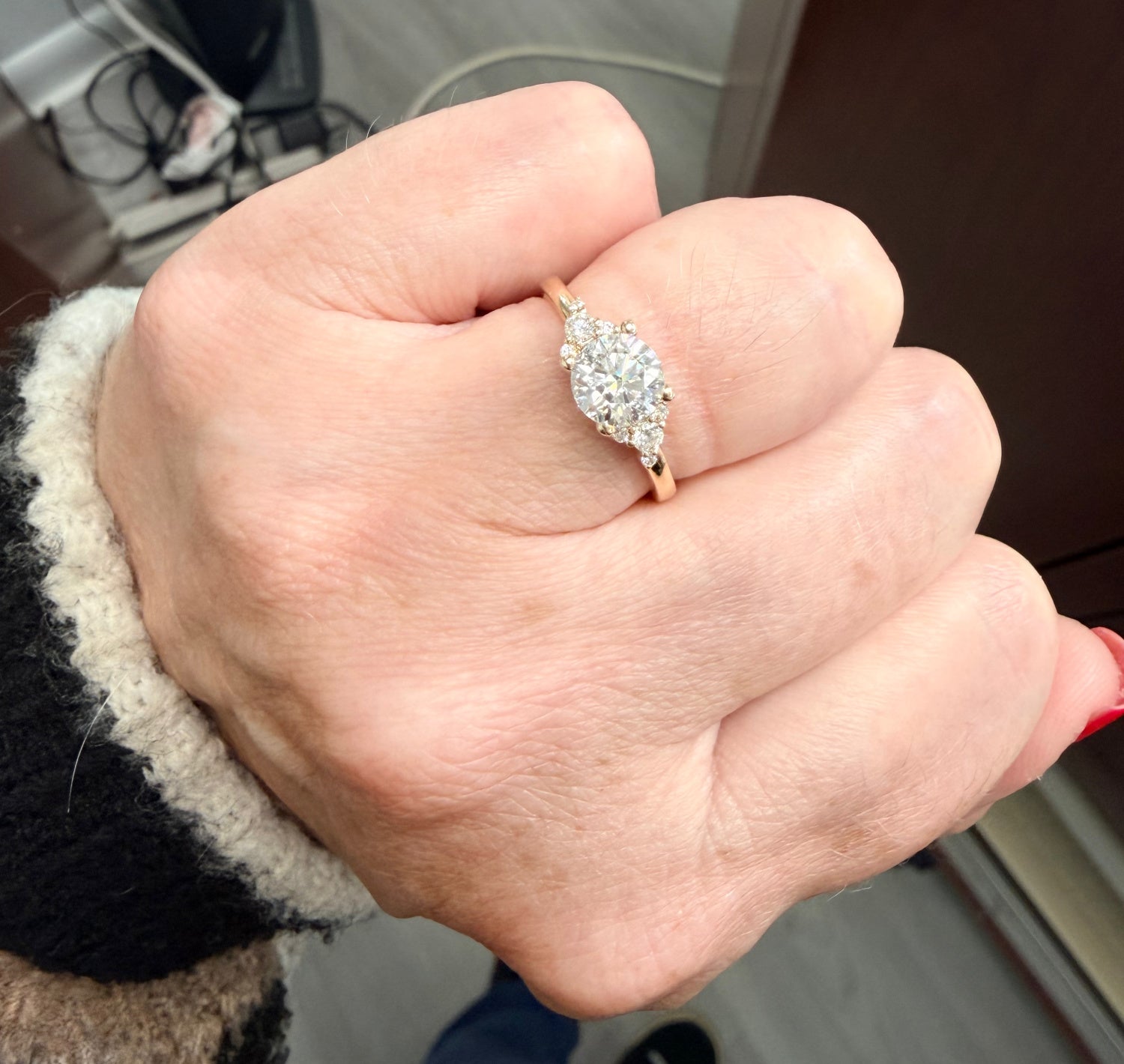 Hand wearing a diamond engagement ring with a blurred indoor background