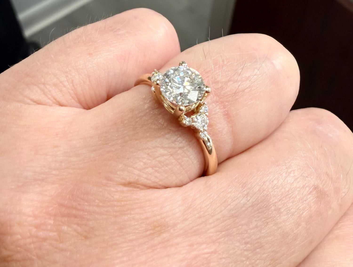 Angled close up view of a  gold engagement ring with a diamond on a hand