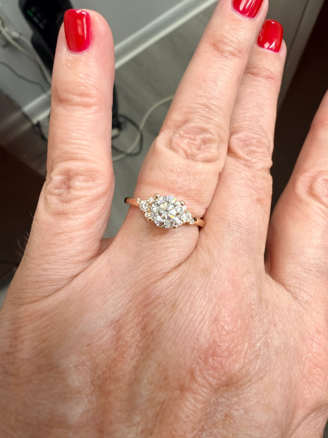 Hand wearing a diamond engagement ring with red nail polish on a blurred background