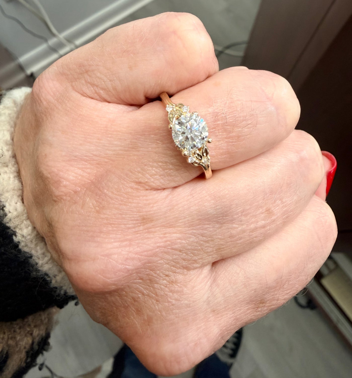 Hand wearing a gold  engagement ring with a large round diamond, blurred background