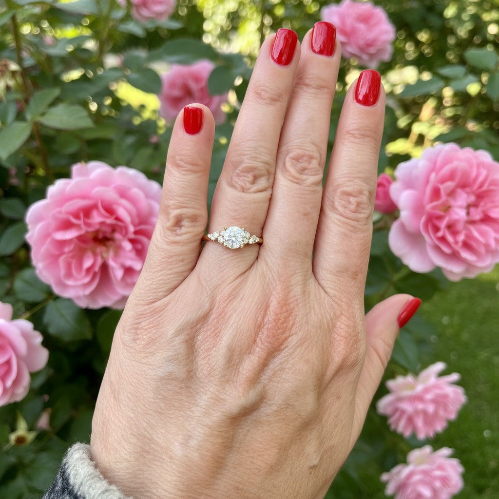 Hand wearing a diamond engagement ring with pink flowers in the background