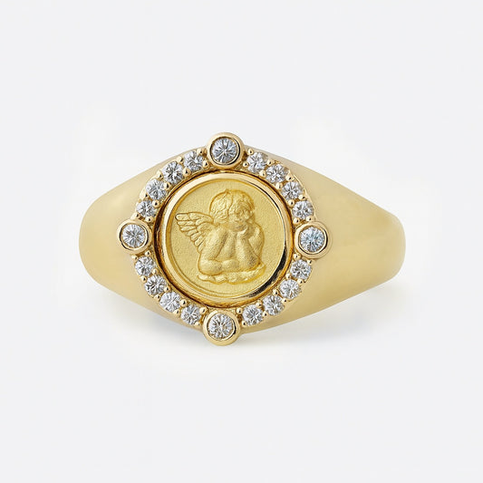 Gold ring with an angel emblem and diamond accents on a white background
