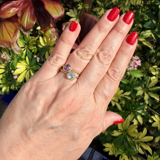 Hand wearing a ring with gemstones against a green leafy background