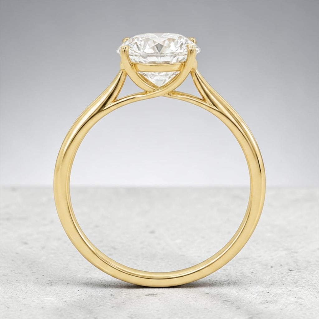 A yellow gold solitaire engagement ring with a round brilliant-cut diamond, shown from a front-facing perspective on a neutral gray background.
