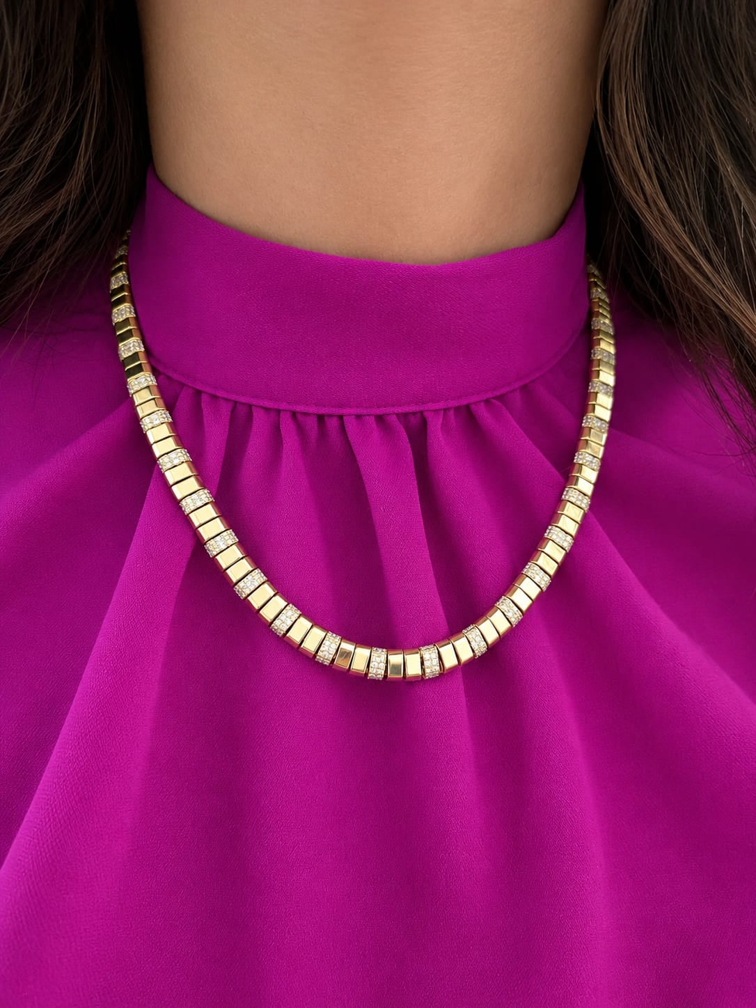A close-up of a 14K yellow gold geometric modern contemporary diamond necklace worn by a model in a bright magenta dress.