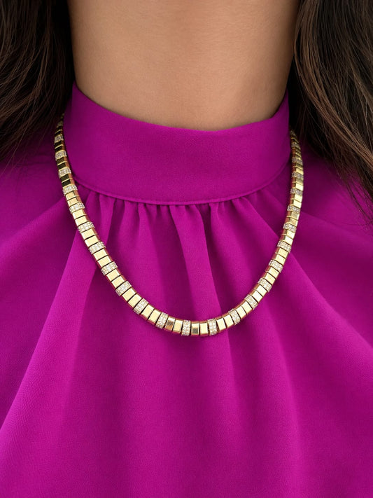 A close-up of a 14K yellow gold geometric modern contemporary diamond necklace worn by a model in a bright magenta dress.