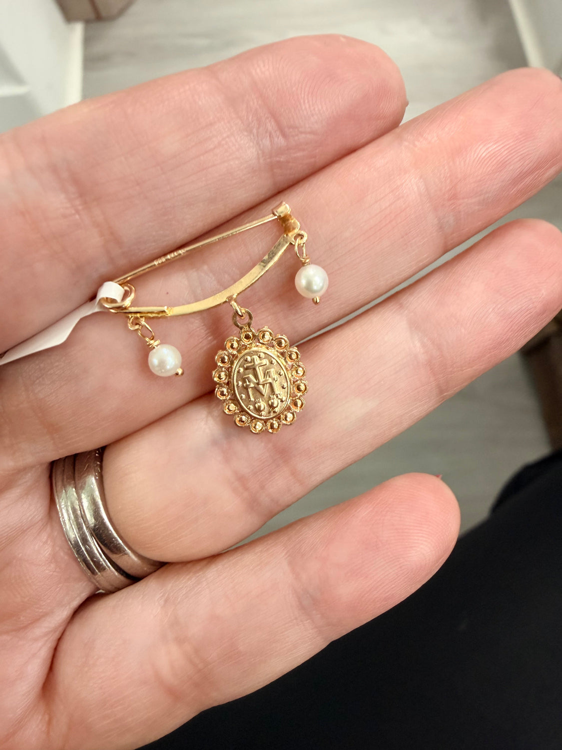 A gold-tone brooch with a central oval medallion and two small pearl-like drops, shown resting on a person's hand.