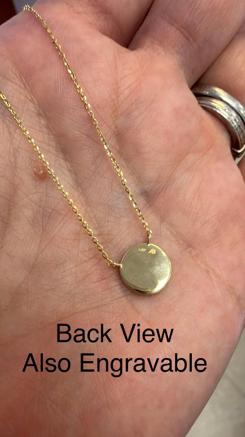 A close-up of a gold chain necklace with a round disc pendant resting on an open hand. The text 'Back View Also Engravable' is overlaid at the bottom.