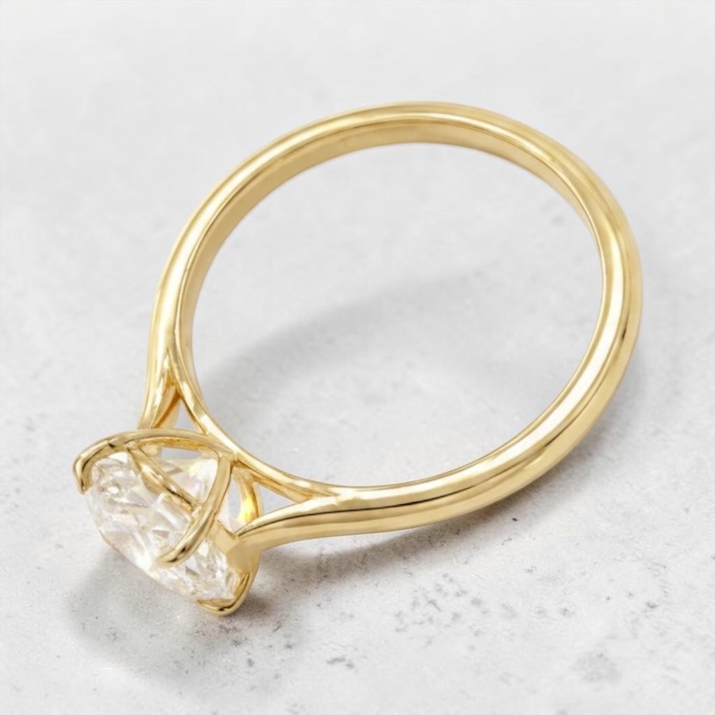 A yellow gold ring with a large, basket-four prong setting with a diamond gemstone, photographed on a light gray textured surface.