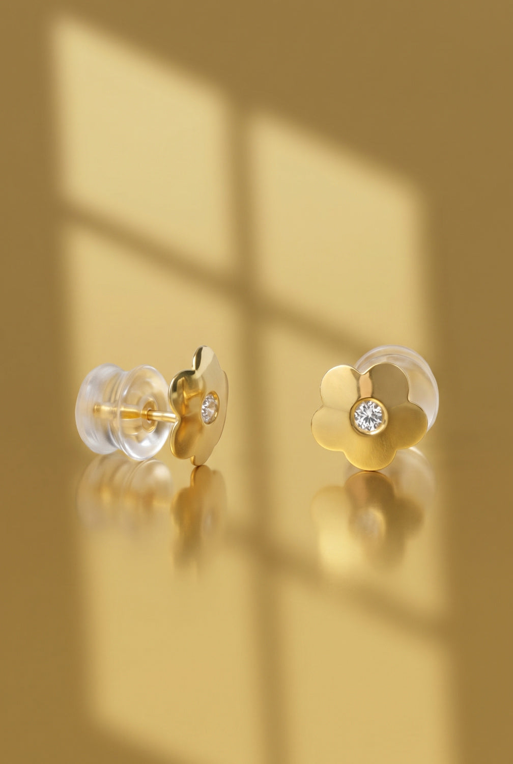 Flower-shaped earrings with clear silicon backs and gold components on a reflective surface.