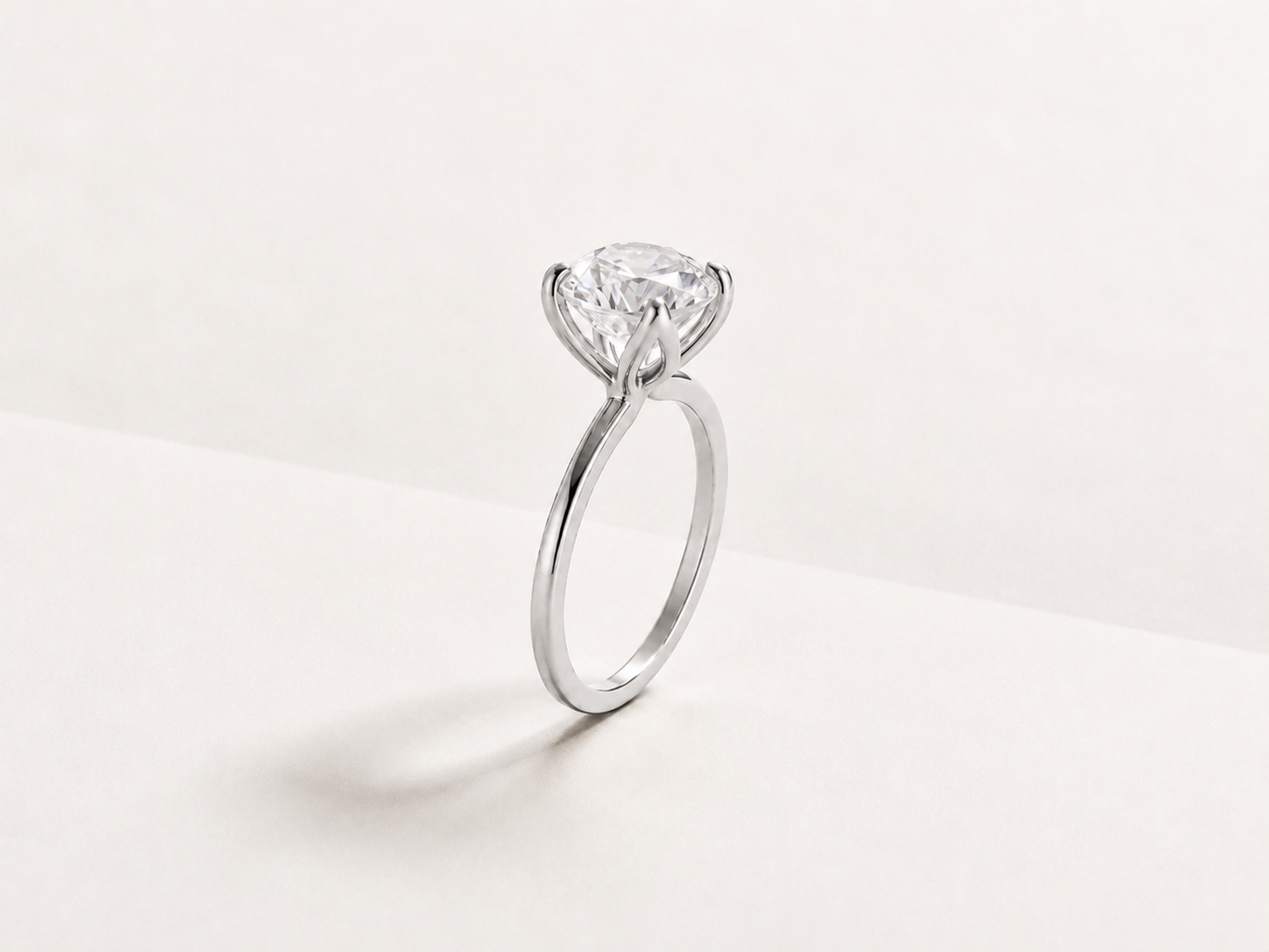 A classic solitaire engagement ring featuring a round brilliant-cut diamond set in a white gold metal band, photographed on a clean, light off-white background.
