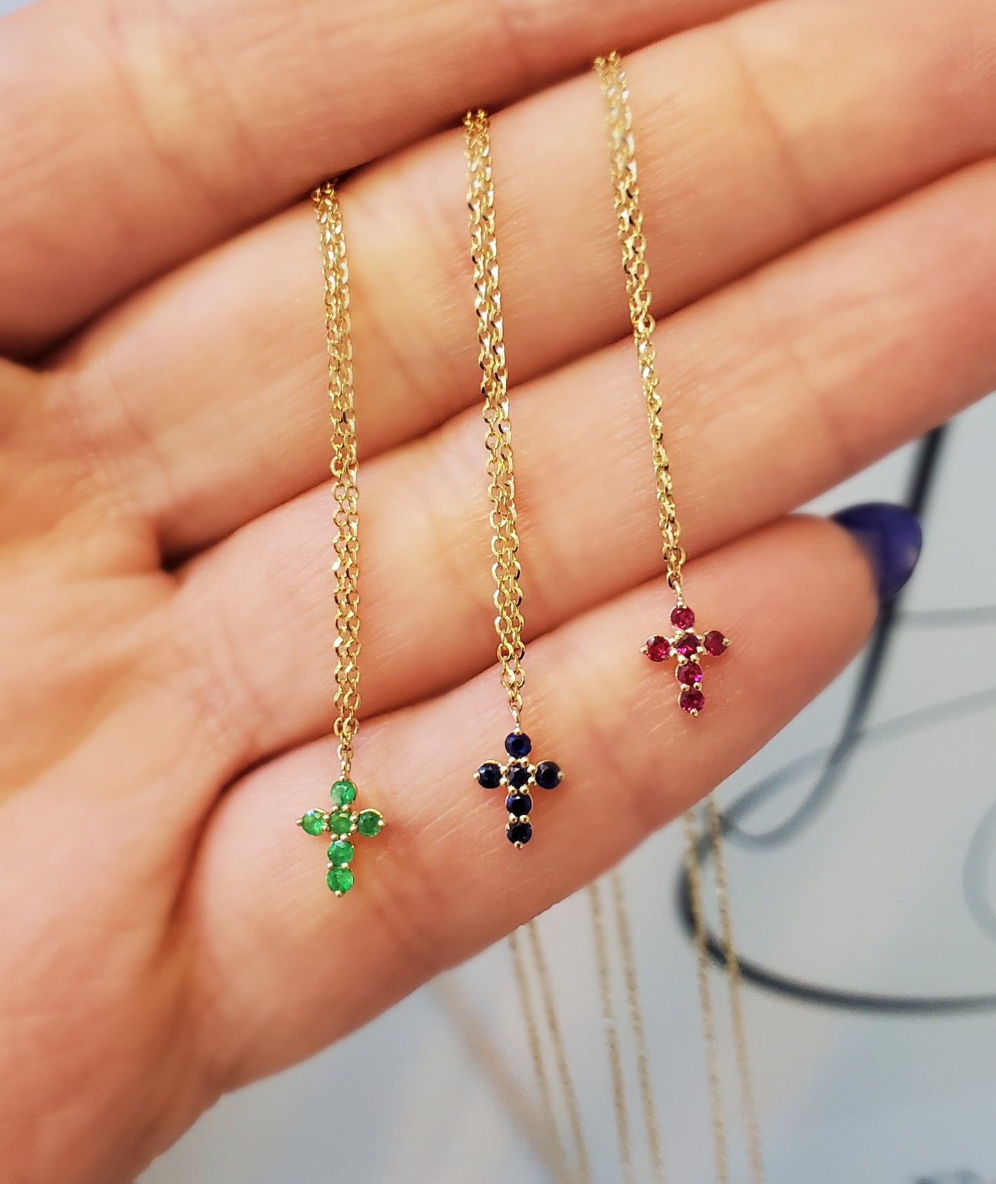 Three gold cross-shaped necklaces with gemstones on a hand.
