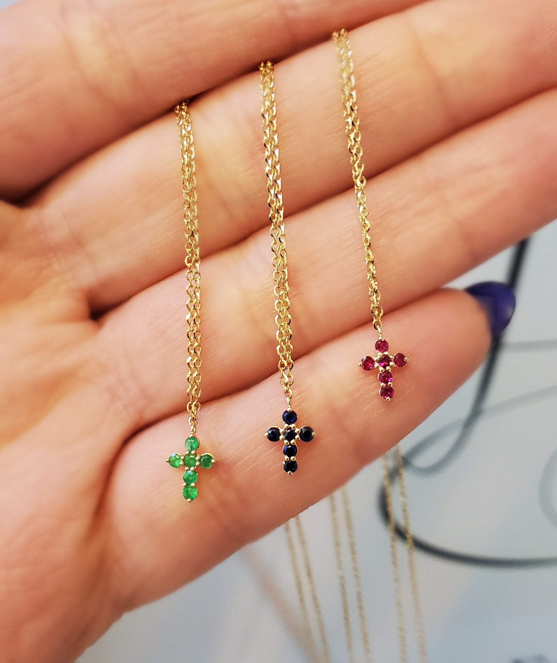 Three gold cross-shaped necklaces with gemstones on a hand.