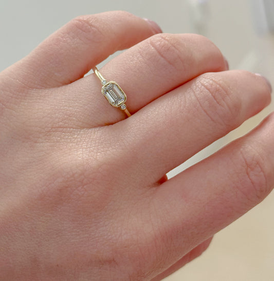 Gold ring with a diamond on a person's finger against a neutral background