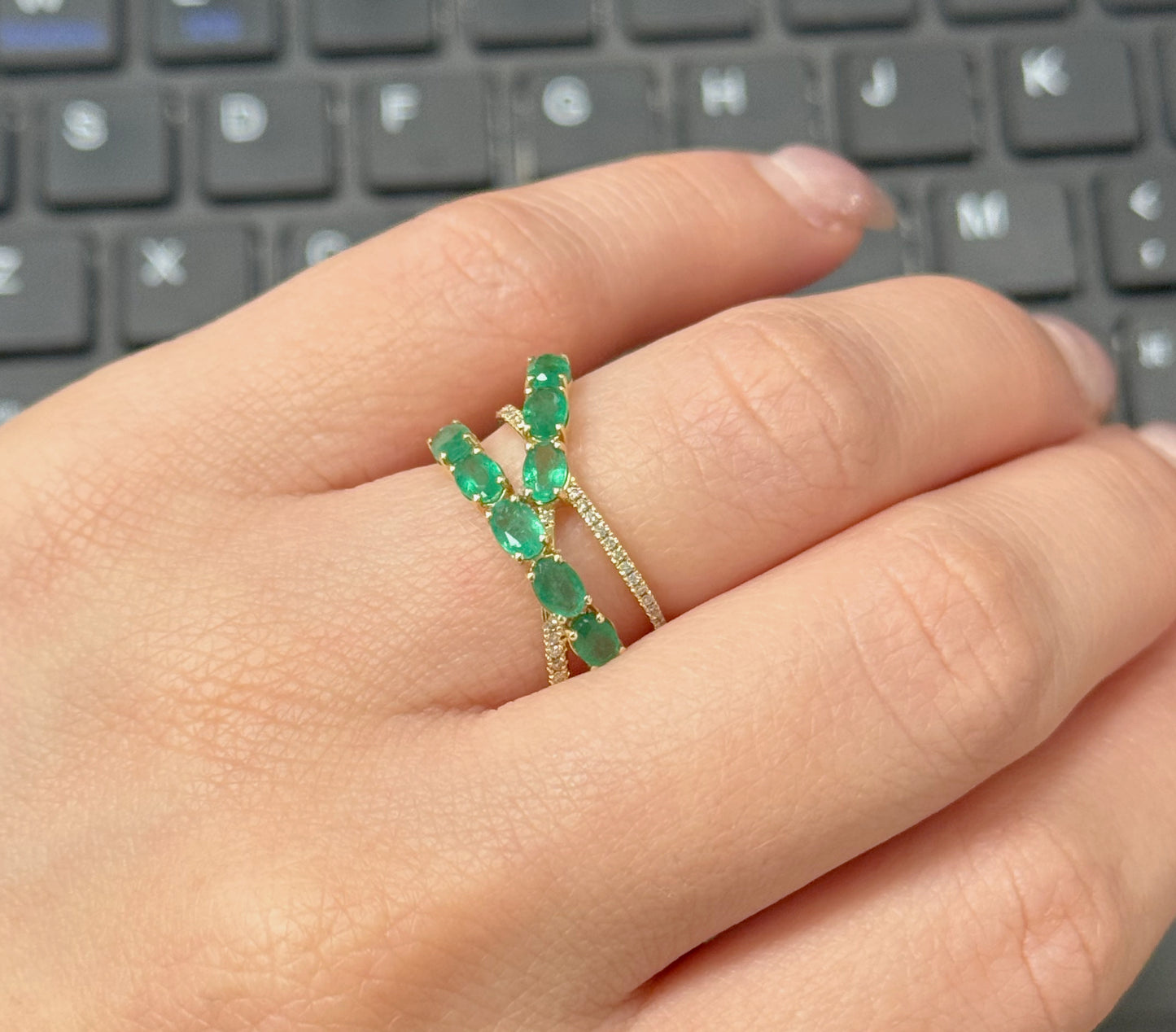 Hand wearing a green emerald ring with a keyboard in the background