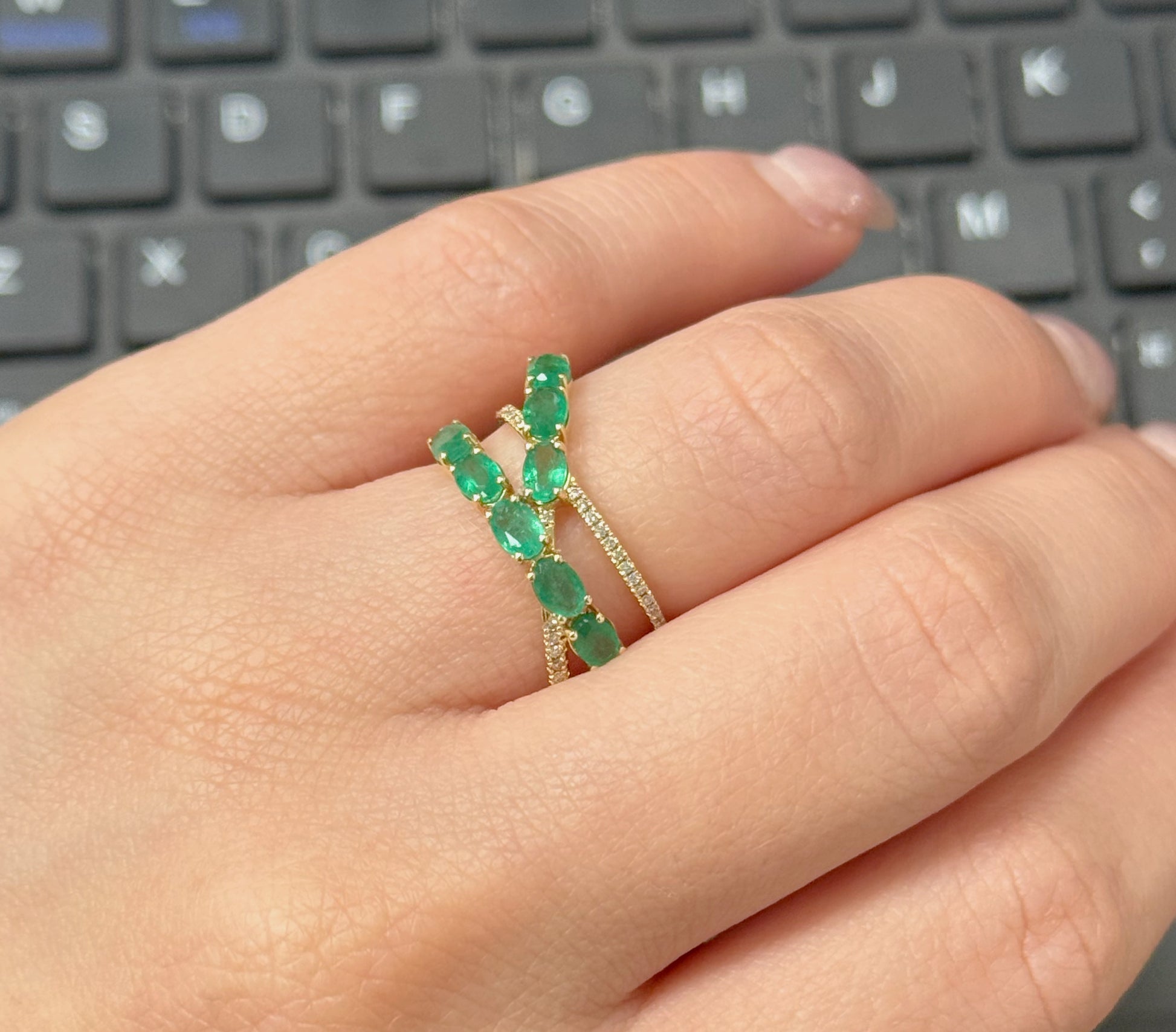 Hand wearing a green emerald ring with a keyboard in the background