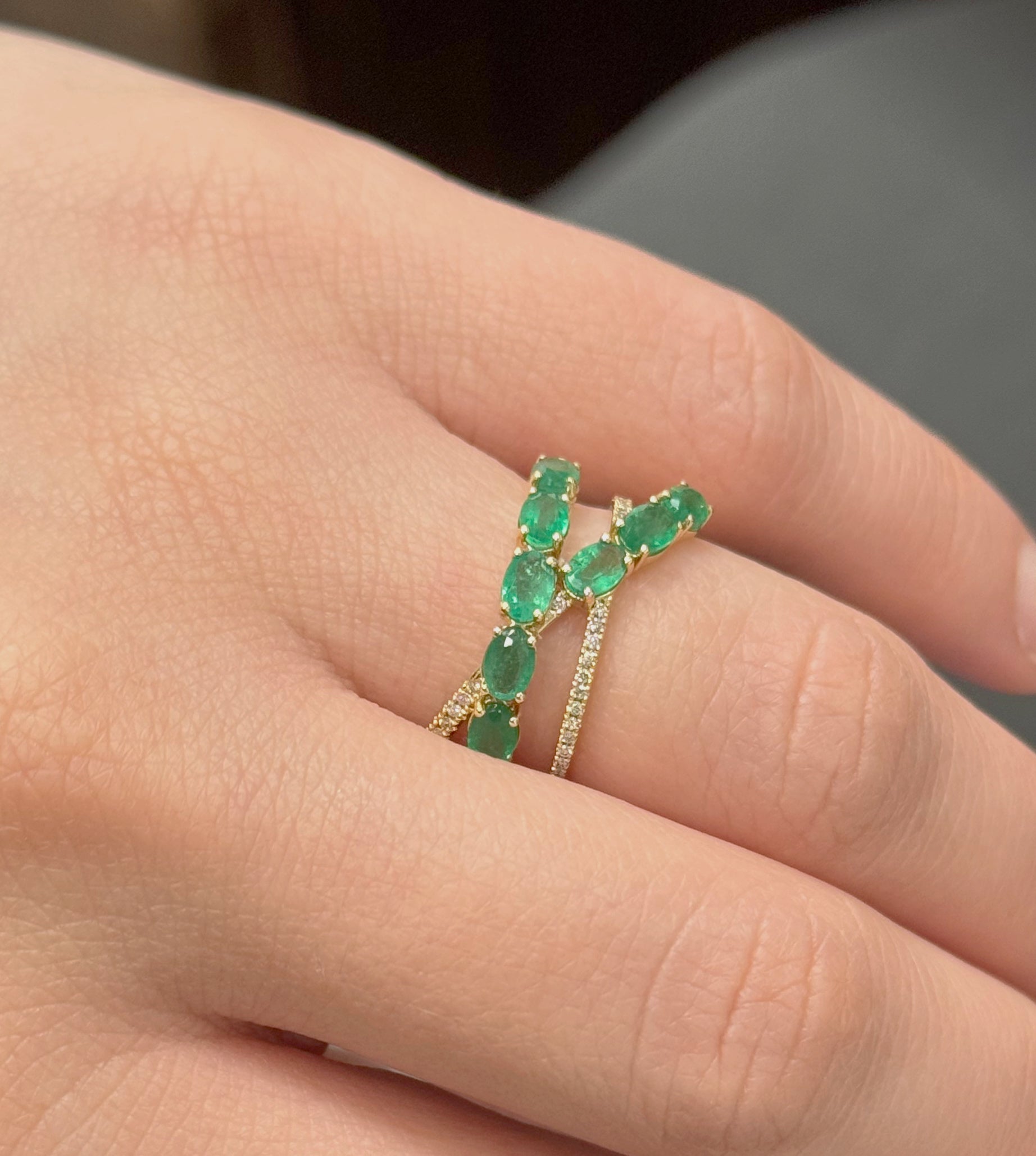 Close-up of a hand wearing a green emerald ring with a blurred background