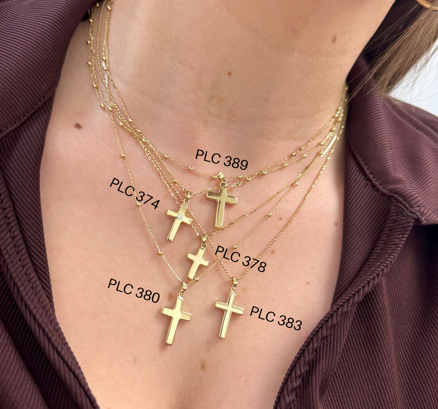 Gold cross necklaces with visible labels on a person wearing a brown garment.