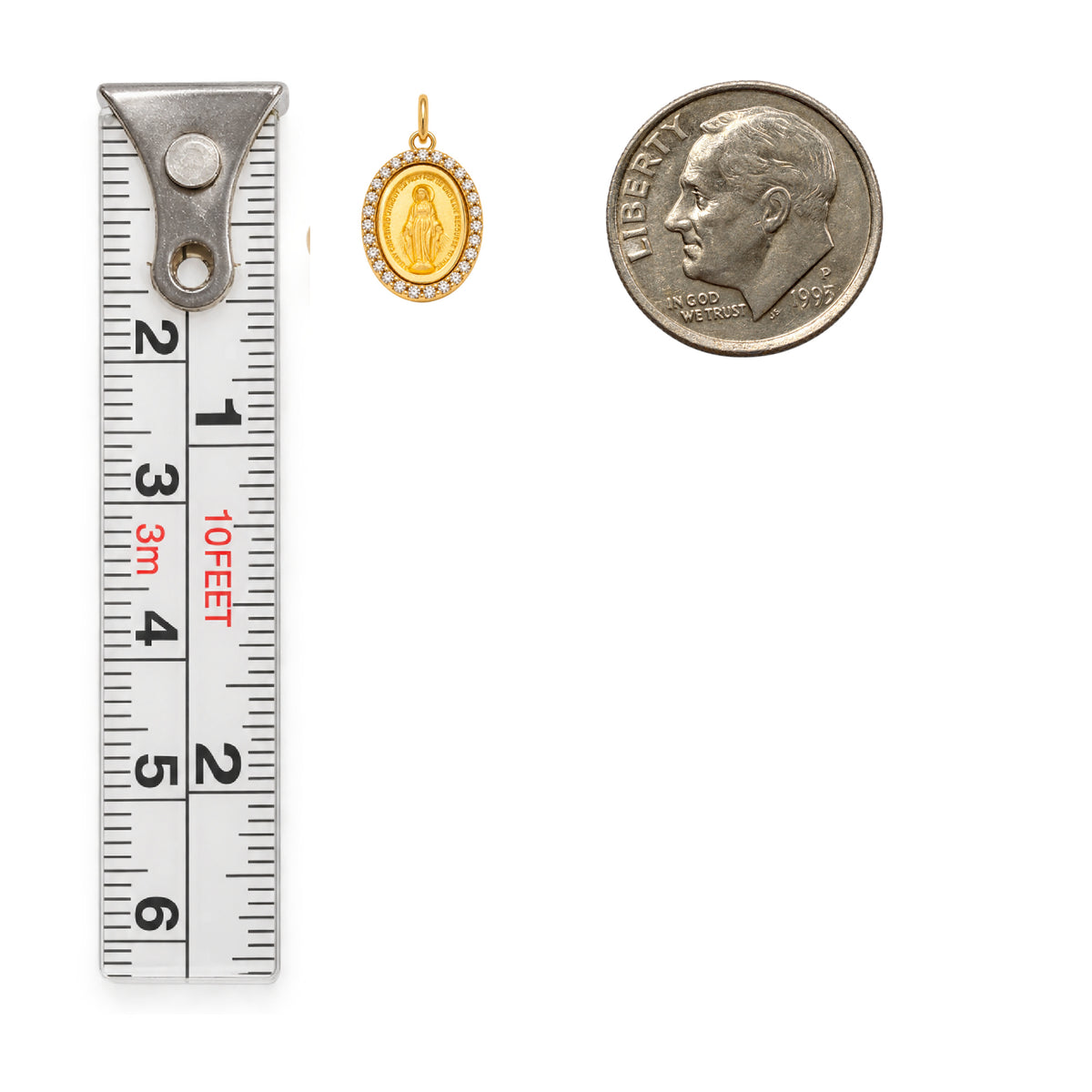 A small gold  Diamond Miraculous religious pendant shown next to a metal tape measure and a U.S. Dime Coin