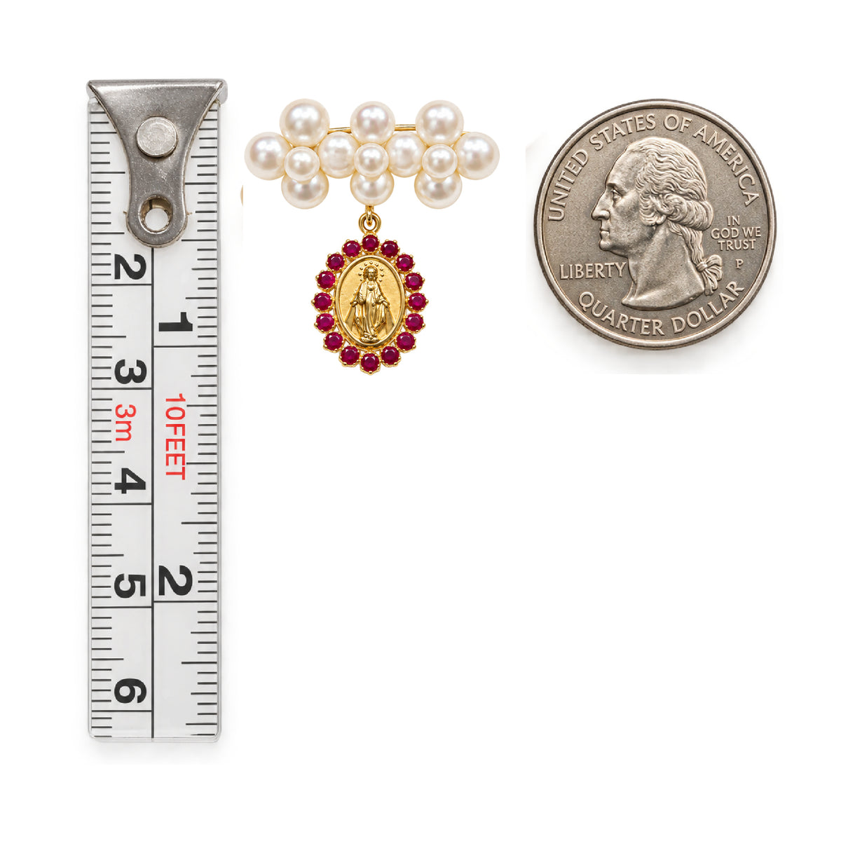 A gold and ruby pendant necklace with a pearl collar is shown next to a silver measuring tape and a US quarter dollar coin for scale, on a white background.