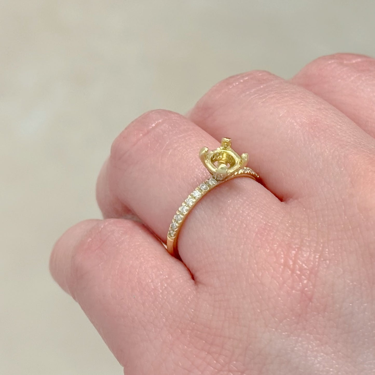 Gold ring with a diamond on a finger against a neutral background