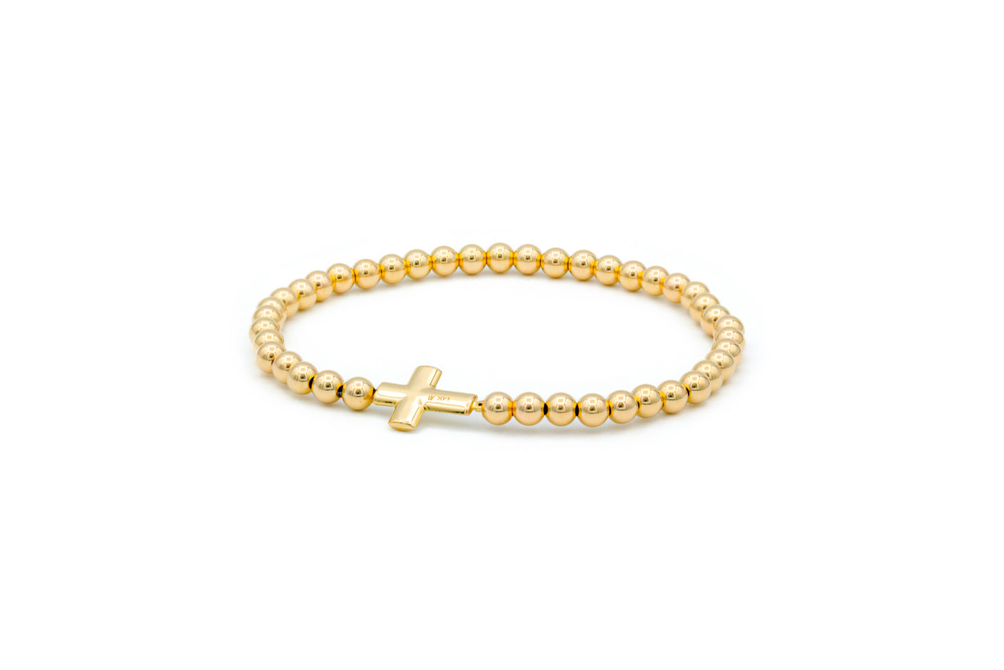 A gold beaded elastic bracelet with a solid gold puff cross charm.