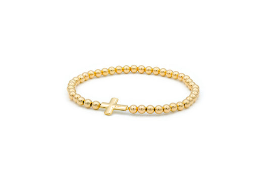 A gold beaded elastic bracelet with a solid gold puff cross charm.