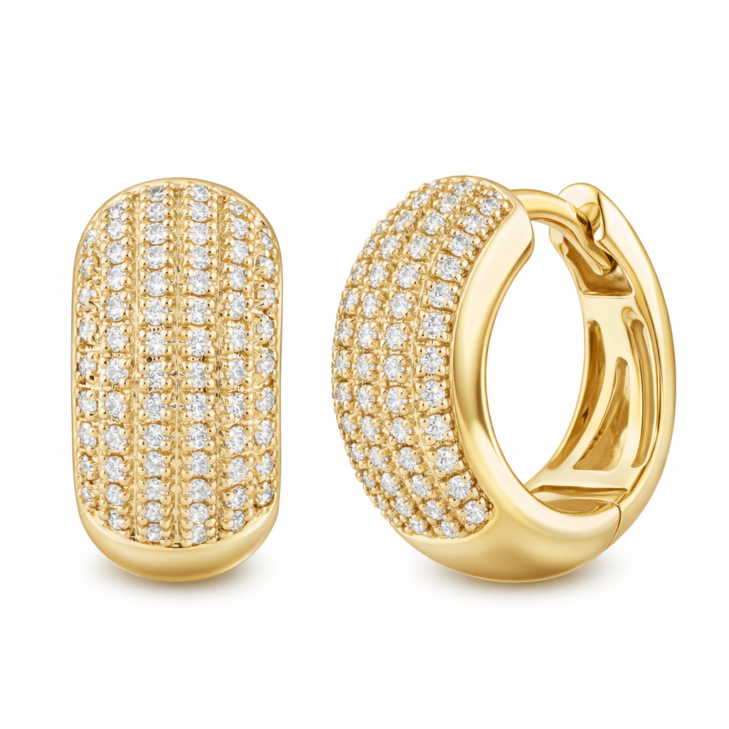 A pair of 14K gold dome pave diamond huggie earrings with a uniform sparkle pattern created by the arranged diamonds.