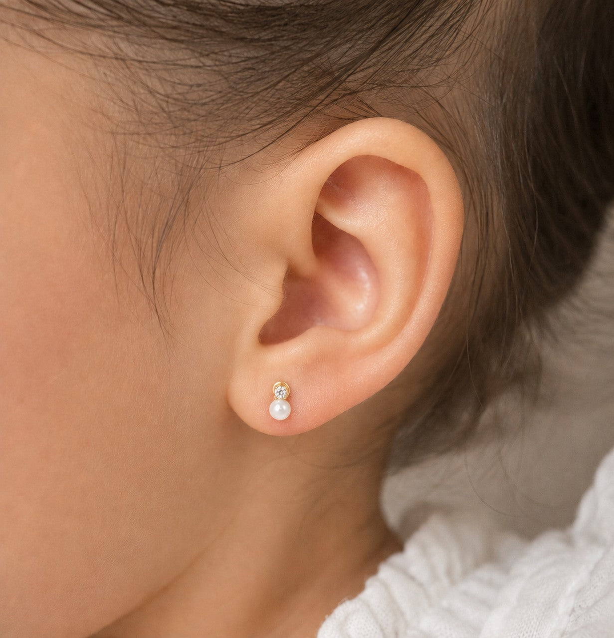 Close-up of an ear wearing a pearl earring with a neutral background