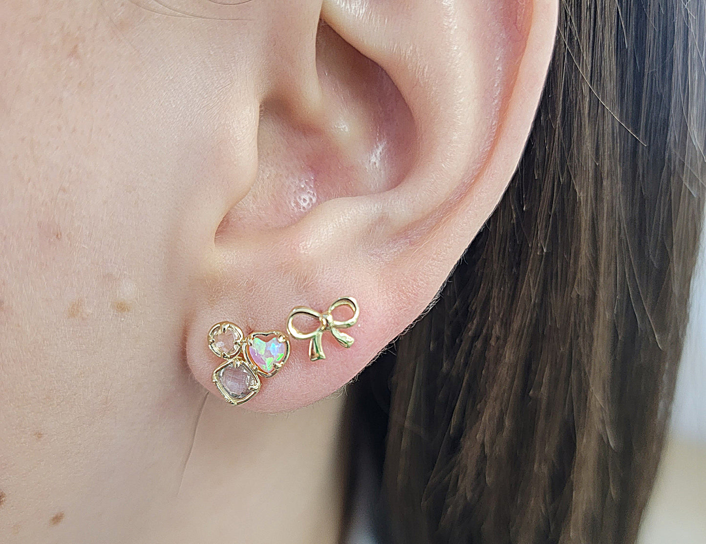 Close-up of an ear wearing a gold bow-shaped earring with heart details.