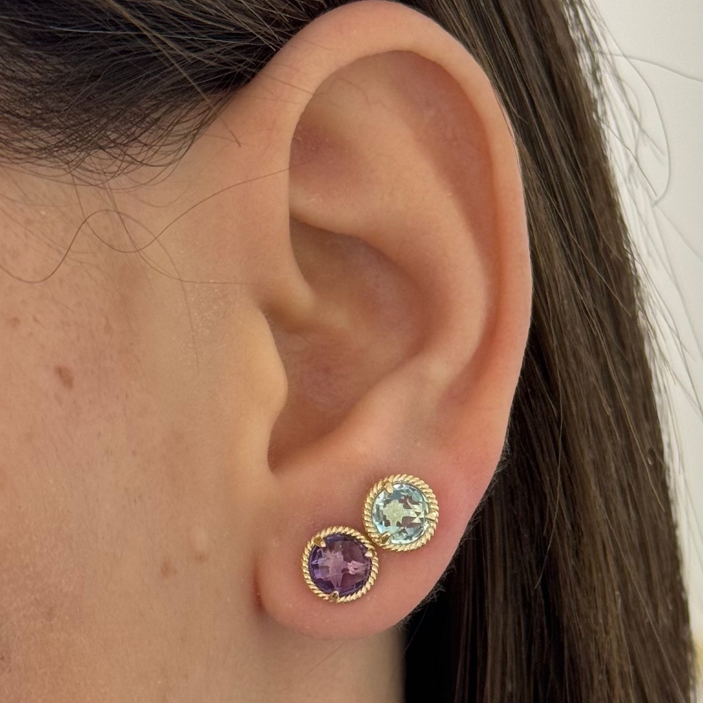 Close-up of an ear wearing two round amethyst and blue topaz gemstone earrings.