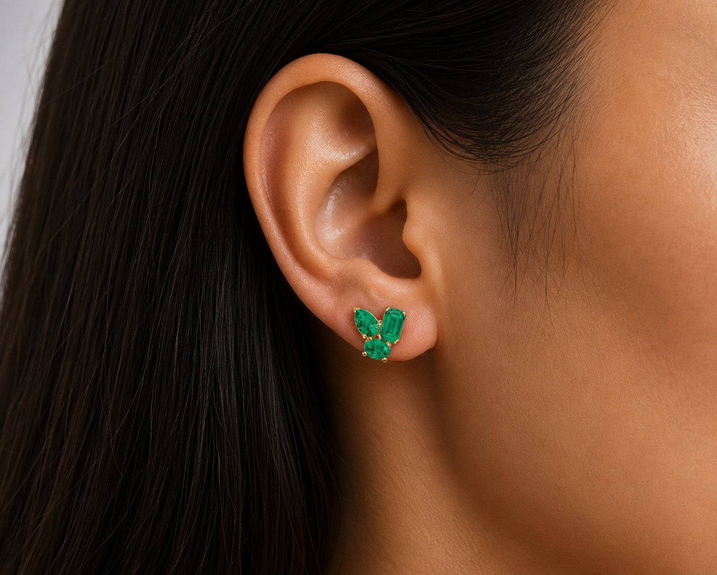 Close-up of an ear wearing a green emerald gemstone earring with a blurred background