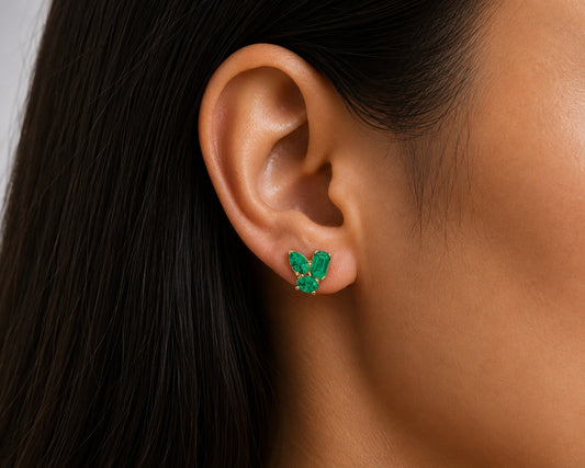 Close-up of an ear wearing a green emerald gemstone earring with a blurred background