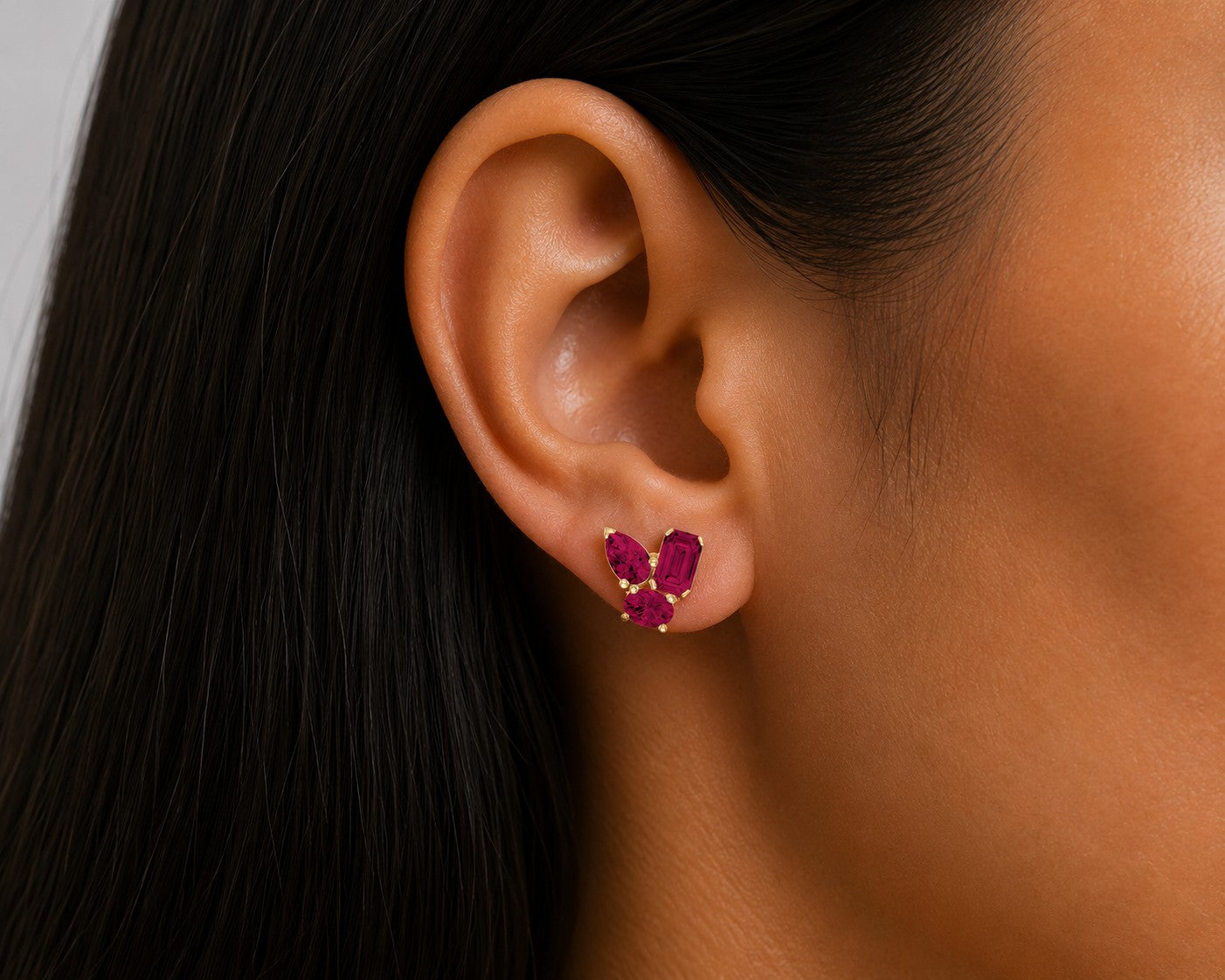 Close-up of an ear wearing a pair of red ruby gemstone earrings with a blurred background