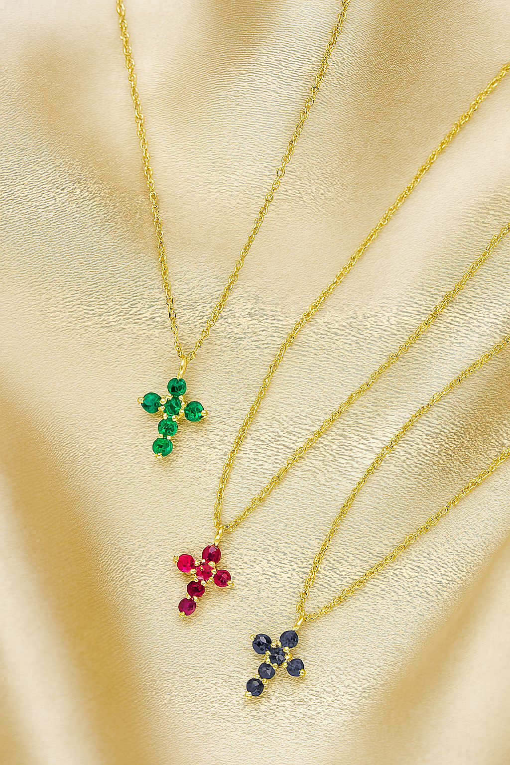 Three gold necklaces with gemstone crosses pendants on a beige fabric background