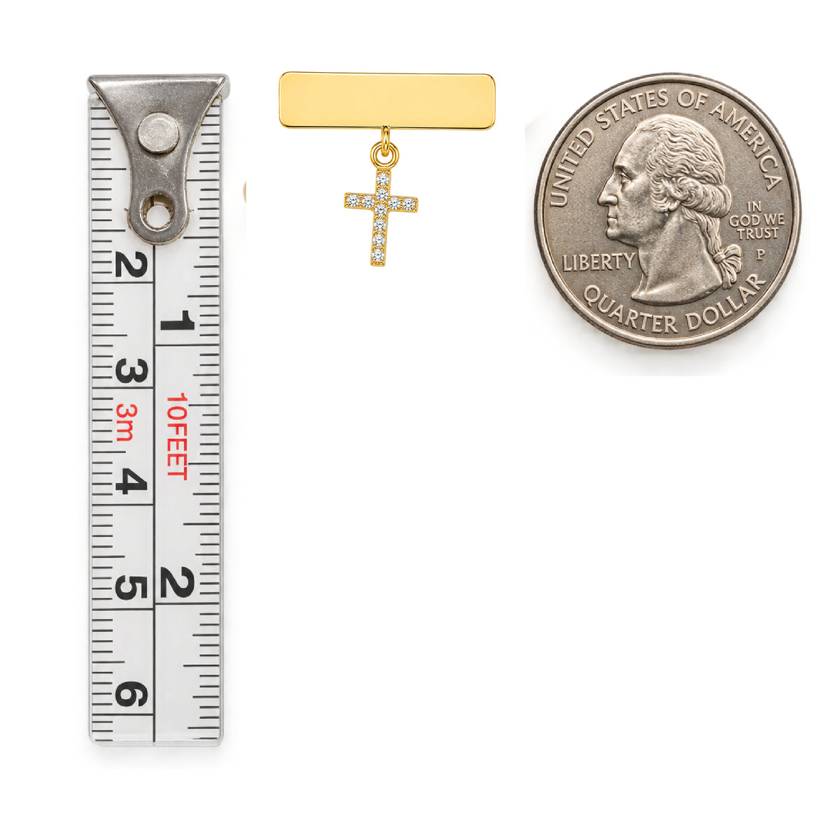 A small gold cross pendant with cubic zirconia stones and a gold engravable bar, shown next to a metal measuring tape measured and a U.S. quarter coin