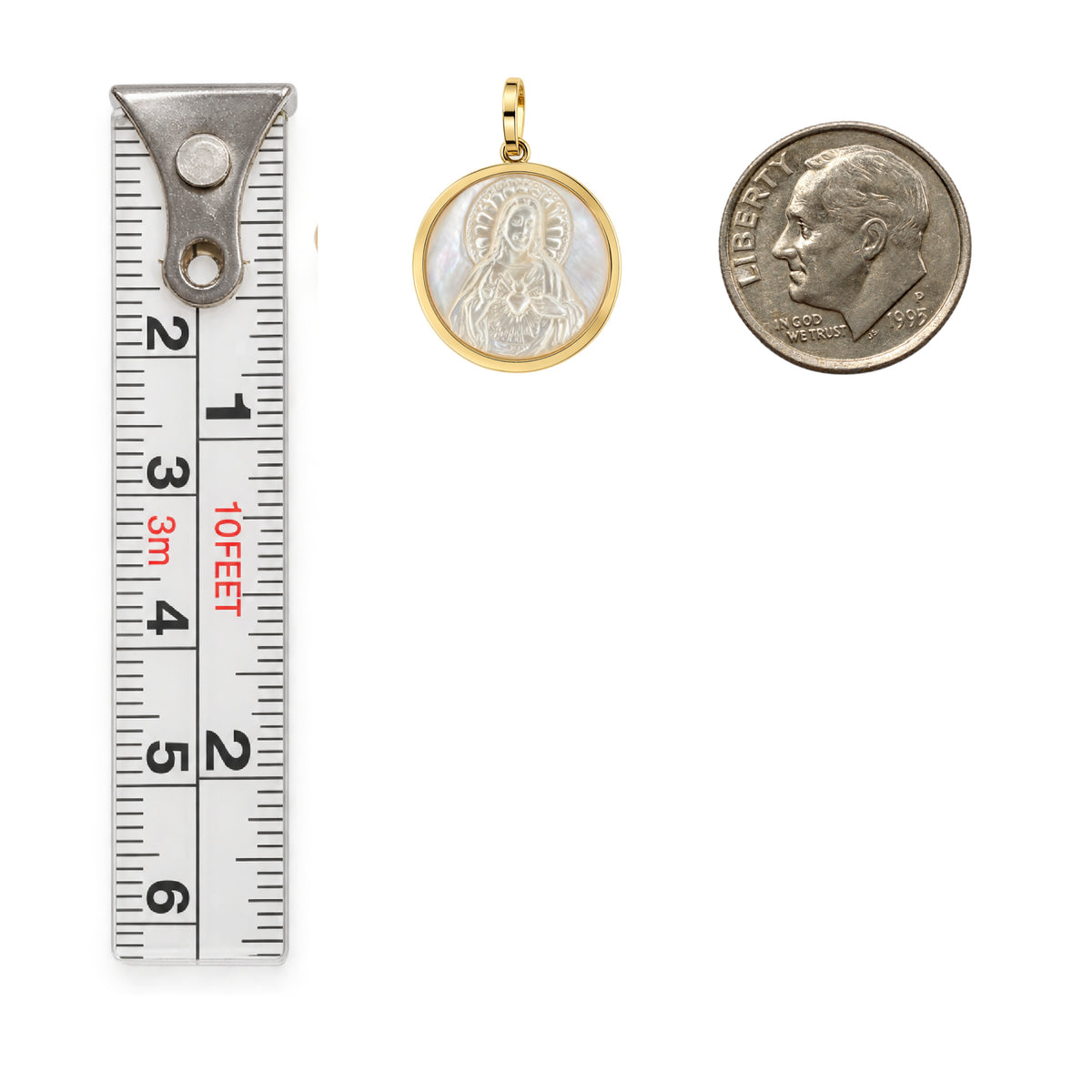 A round gold and white mother-of-pearl Sacred Heart of Jesus pendant shown next to a 10-inch ruler and a dime for scale, on a plain white background.