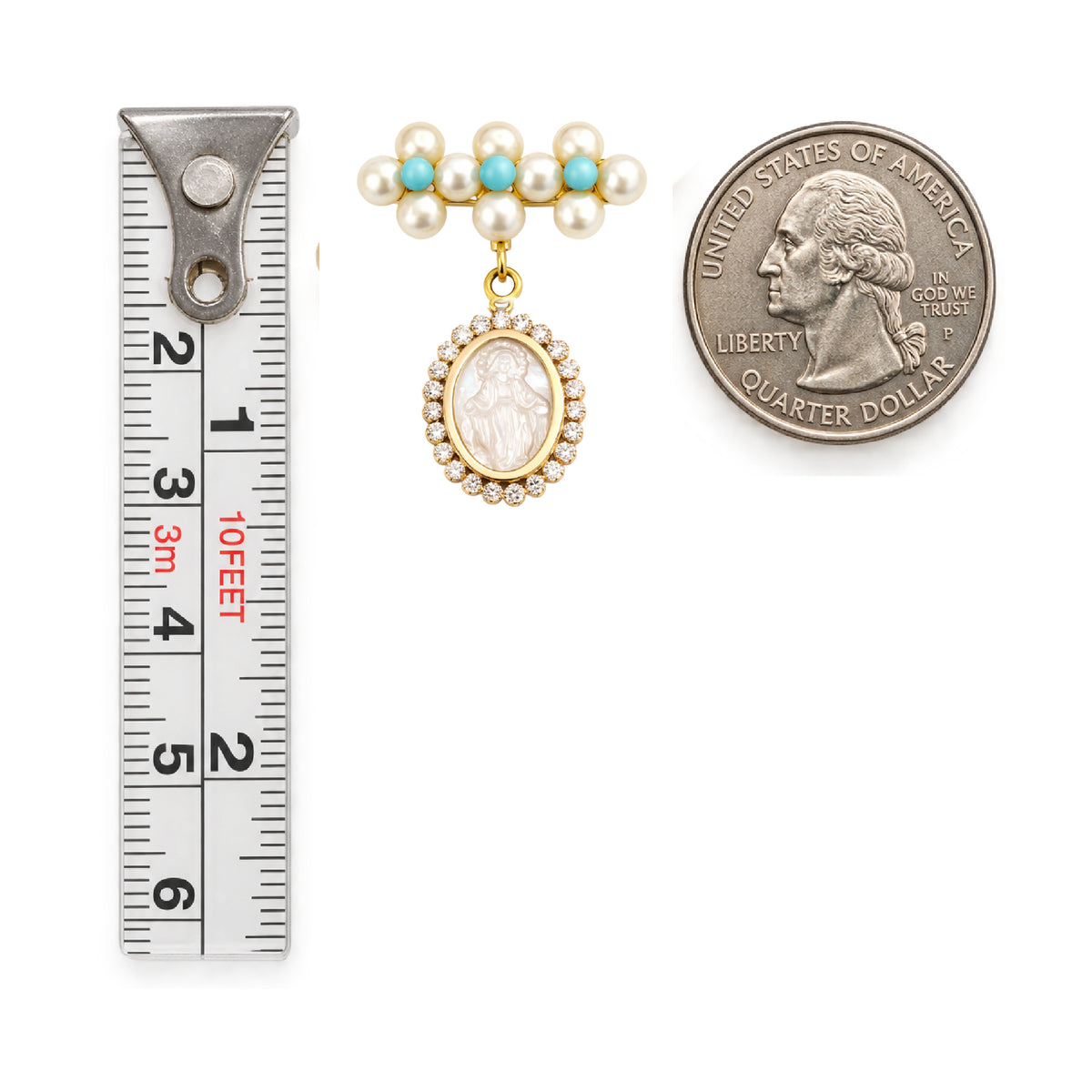 A vintage-style pearl and turquoise brooch with a dangling oval mother of pearl Miraculous pendant with cubic zirconia halo, shown next to a metal ruler for scale and a U.S. Quarter Coin