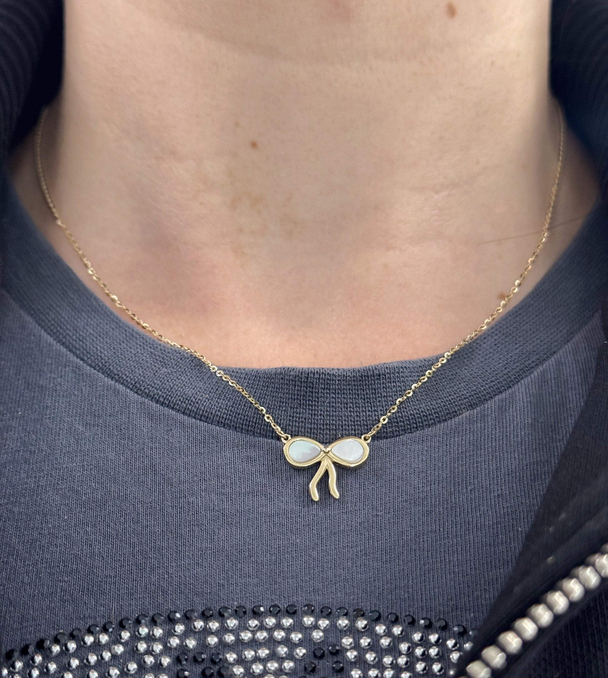 Necklace with a bow-shaped pendant worn by a person against a dark blue garment.
