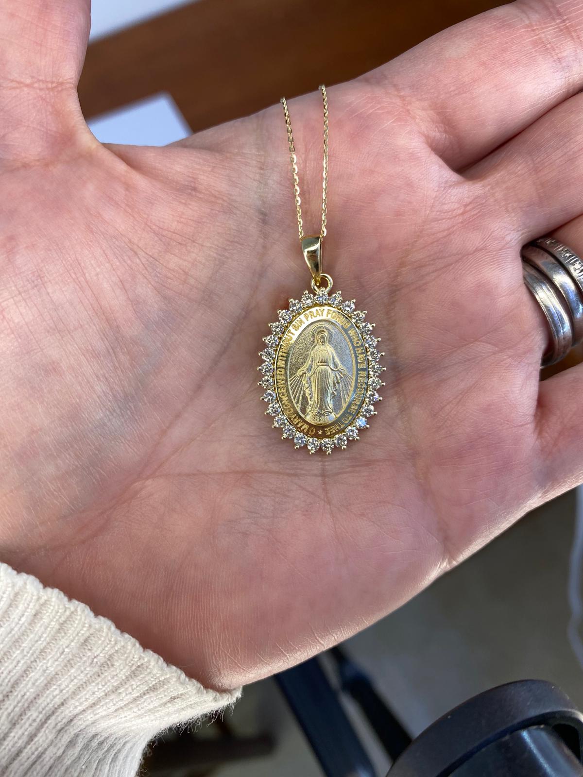 Gold pendant with a religious figure held in a hand