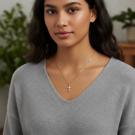 Woman wearing a gray sweater and gold necklace with a cross pendant indoors.
