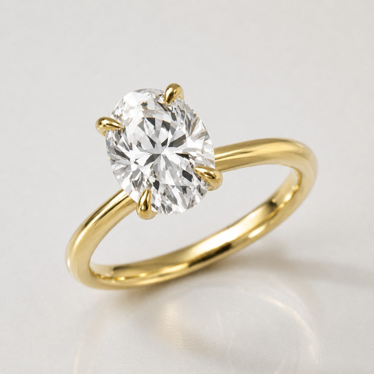 A yellow gold solitaire engagement ring featuring a large oval-cut diamond in a four-prong setting, shown on a clean light gray reflective surface.