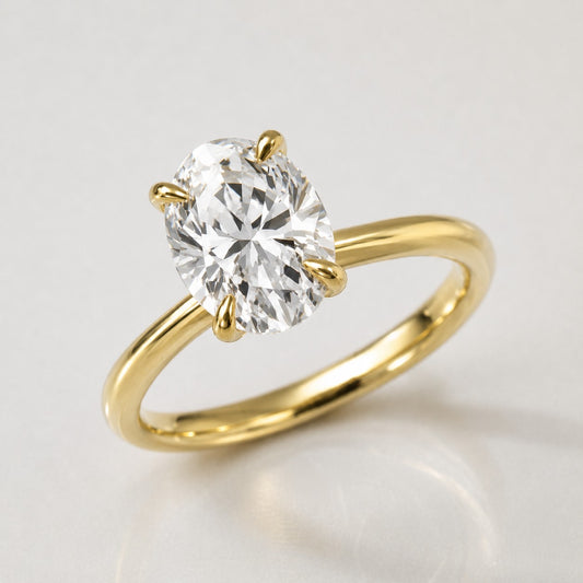 A yellow gold solitaire engagement ring featuring a large oval-cut diamond in a four-prong setting, shown on a clean light gray reflective surface.