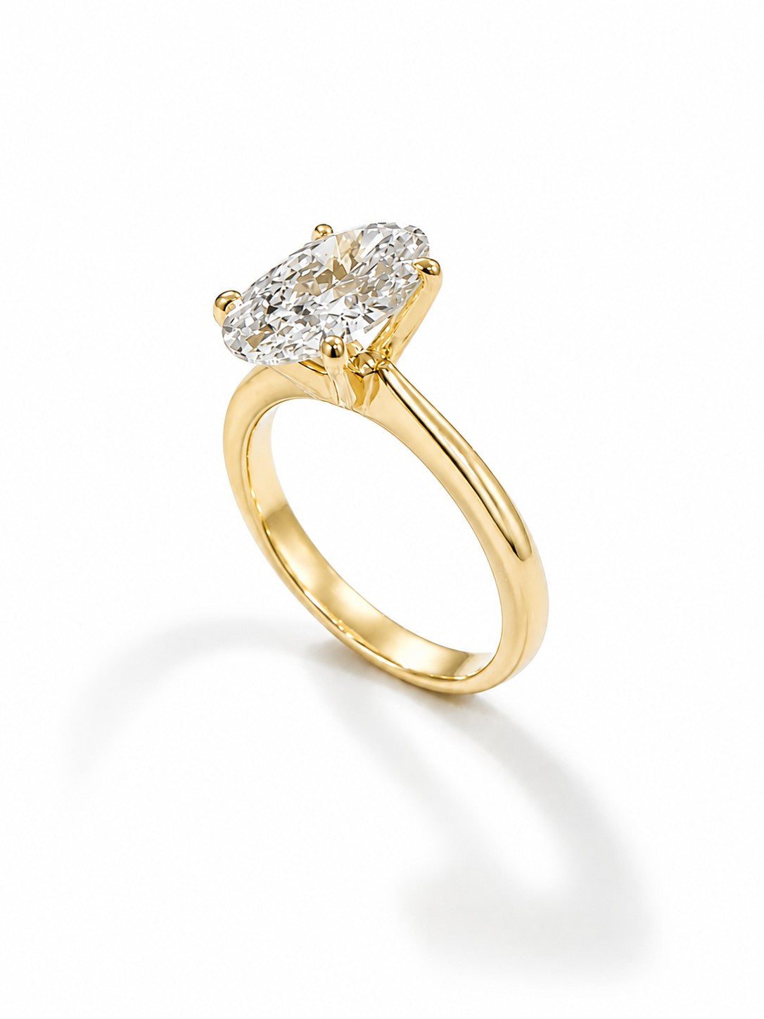 A yellow gold engagement ring with a oval-cut diamond solitaire setting, shown in profile view on a clean white background with a soft shadow.