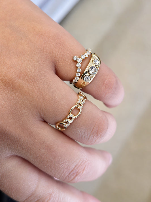 Three gold rings with diamond stones worn on a person's hand, shown in a close-up lifestyle shot against a soft beige background.